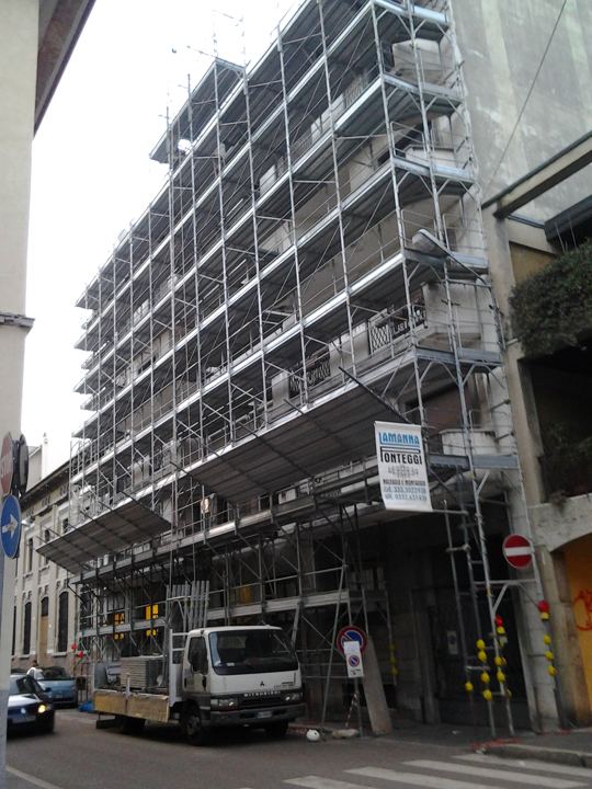 Ponteggio completo su palazzo in centro urbano, con automezzo di cantiere su strada.