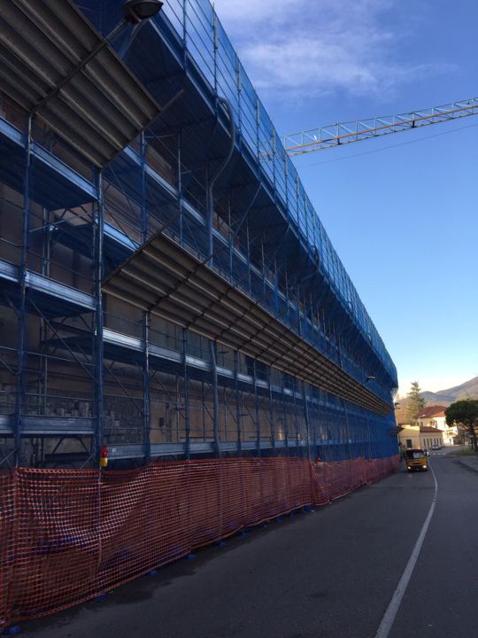 Fronte lungo con rete di protezione blu e gru a torre in cantiere industriale.