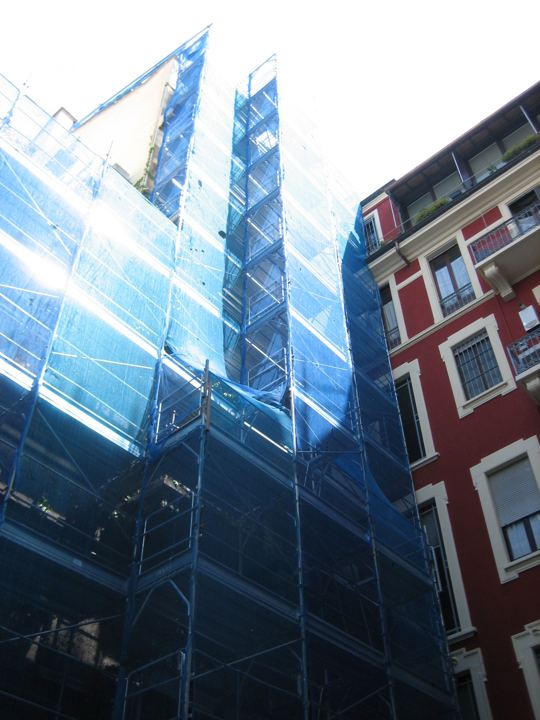 Ponteggio con rete blu su edificio d'angolo.