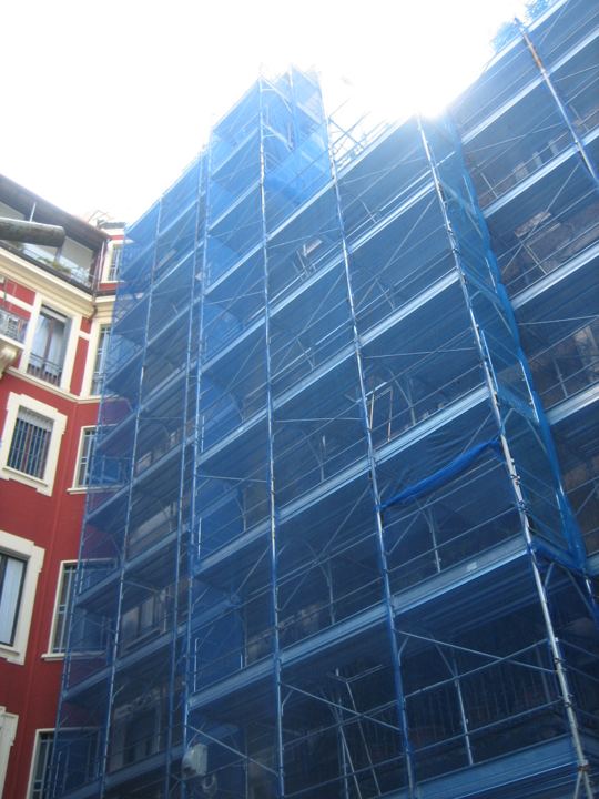 Facciata in ristrutturazione con rete di protezione blu.