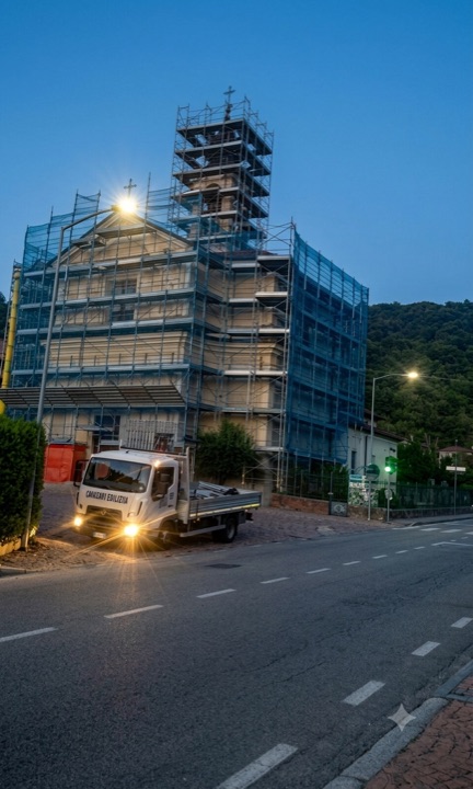 Chiesa con campanile in restauro: ponteggio dedicato su facciata e torre campanaria — cantiere all'imbrunire.
