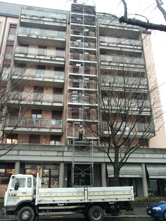 Cantiere su palazzo moderno con autocarro in strada alberata.